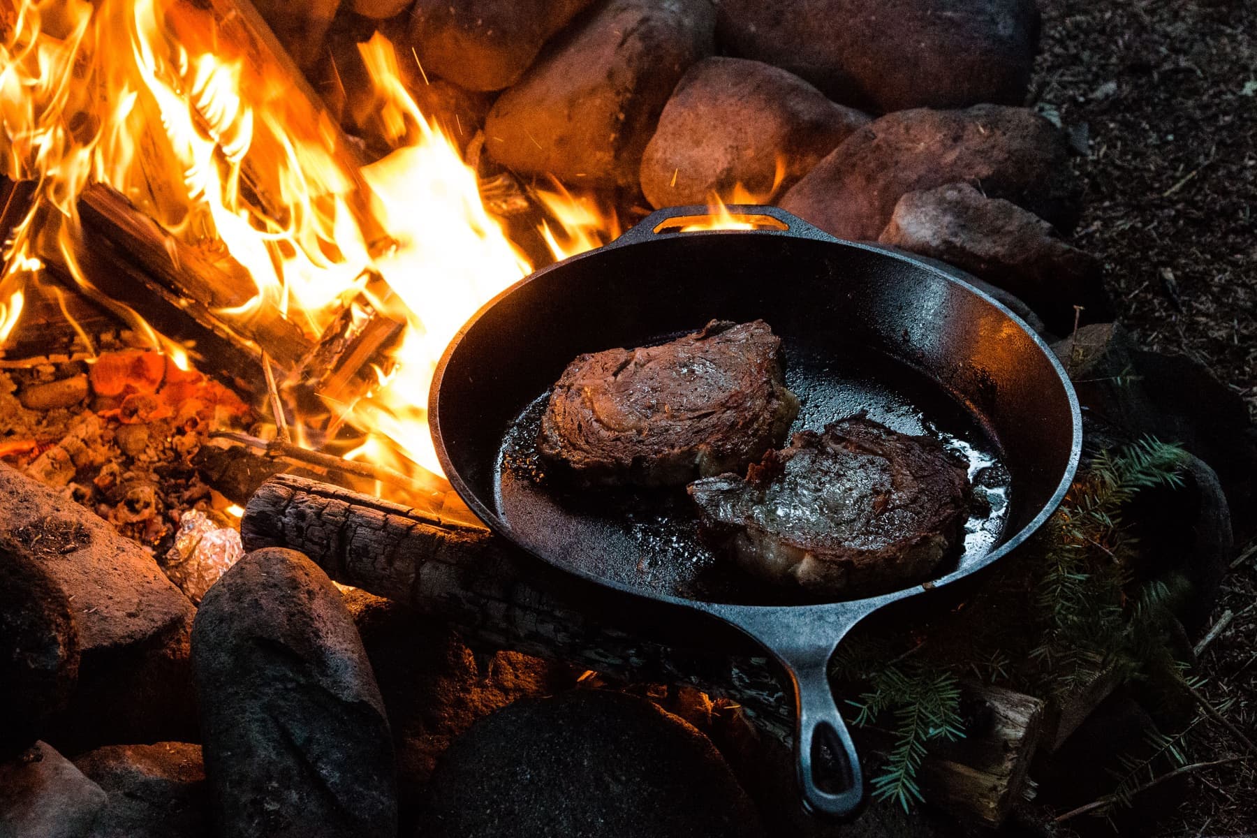 A steak searing in a hot cast iron skillet, the edges browning